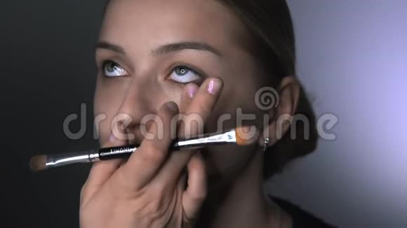 化妆师为美容工作室的年轻女性制作专业化妆化妆师在眼睛上涂抹遮瑕膏视频的预览图
