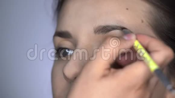 为坐在工作室的美丽而华丽的女人化妆的过程化妆师化妆眉毛视频的预览图