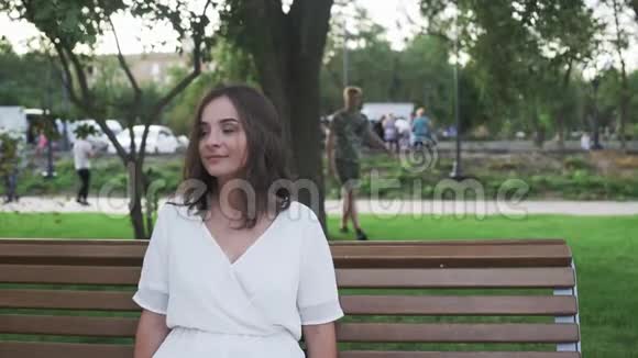 年轻女子坐在长凳上在夏天的公园里等她的男朋友视频的预览图