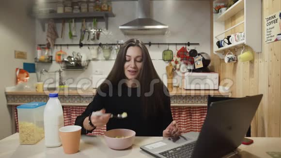 年轻的女人在家里的厨房里工作电脑吃玉米片视频的预览图