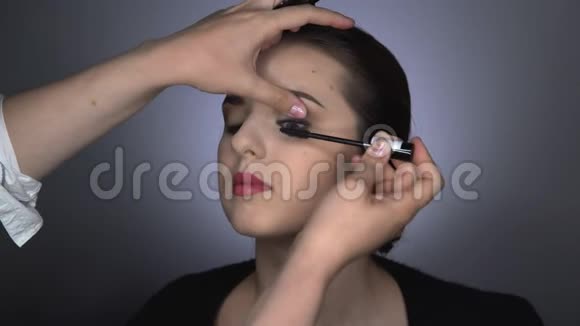 为坐在工作室的漂亮漂亮女人做专业化妆的过程化妆师用睫毛膏视频的预览图