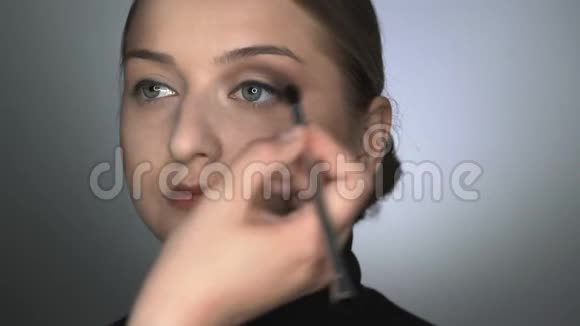 化妆师为美容工作室的年轻女性制作专业化妆化妆师用刷子涂阴影视频的预览图