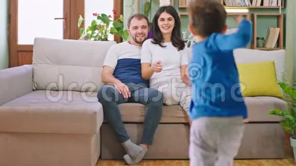 两个孩子和他们年轻的父母玩得很开心坐在沙发上孩子们跑向他们拥抱的父母视频的预览图