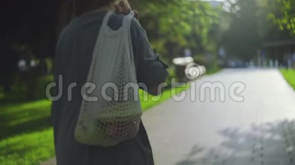 年轻女子肩扛水果棉网购物袋在避暑公园散步视频的预览图