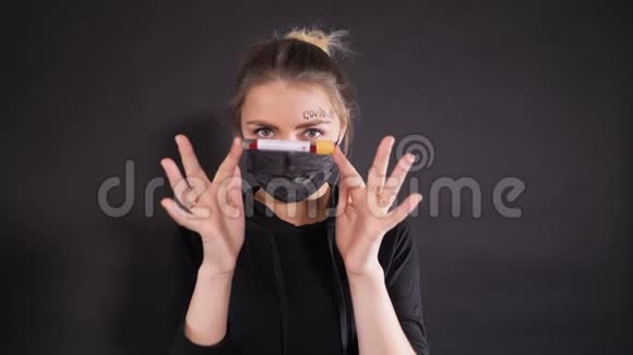 戴着黑色防护面具的女人额头上写着kovid19单词女孩拿着一个试管视频的预览图