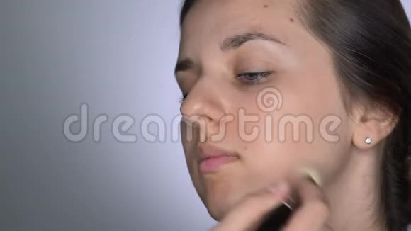 为坐在工作室的美丽而华丽的女人化妆的过程化妆师应用护肤视频的预览图
