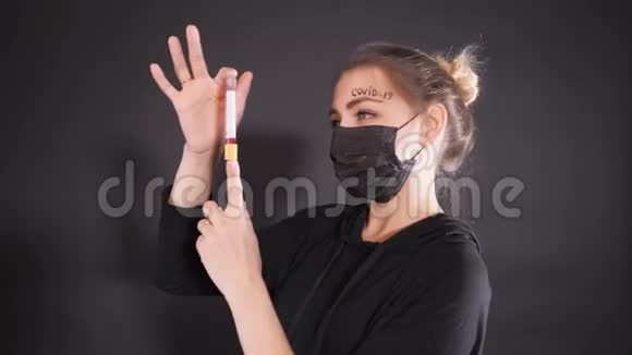 戴着黑色防护面具的女人额头上写着kovid19单词女孩拿着一个试管视频的预览图