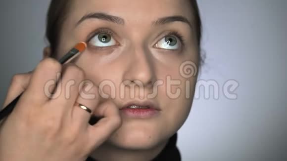 化妆师在美容工作室为年轻女性做专业化妆化妆师在眼睛上涂抹遮瑕膏视频的预览图