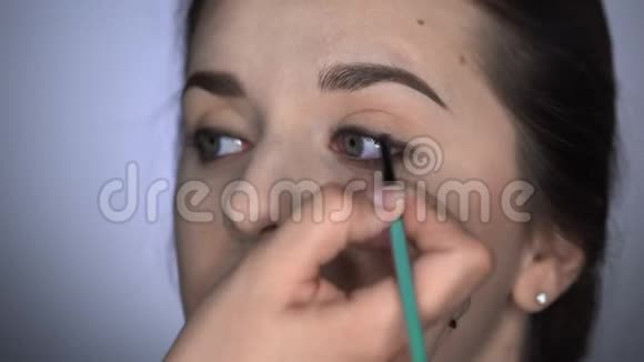 为坐在工作室的漂亮漂亮女人做专业化妆的过程化妆师涂眼线视频的预览图