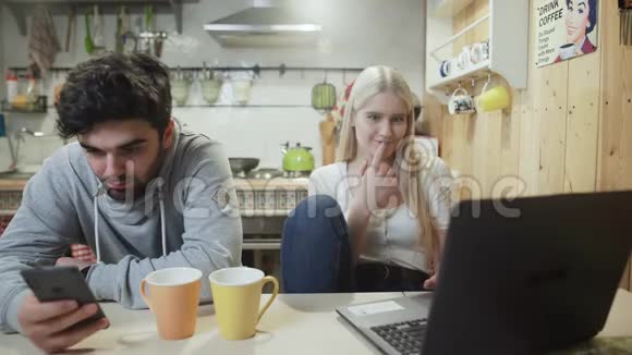 年轻夫妇在厨房里聊天和使用现代笔记本电脑和电话视频的预览图