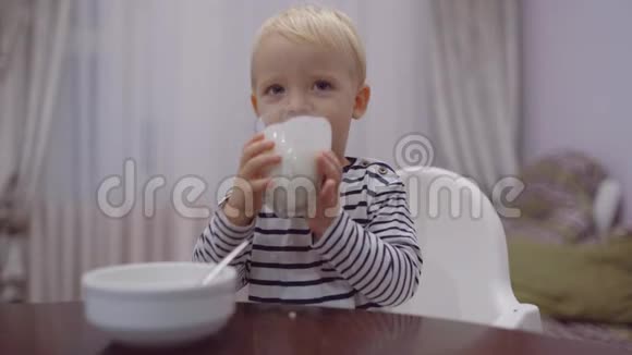 可爱的宝宝吃喝牛奶小男孩喝玻璃牛奶快乐微笑的孩子金发卷曲的孩子视频的预览图