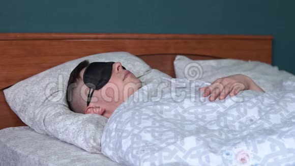 一个年轻人睡在睡眠面具里一个人躺在他房间的床上视频的预览图