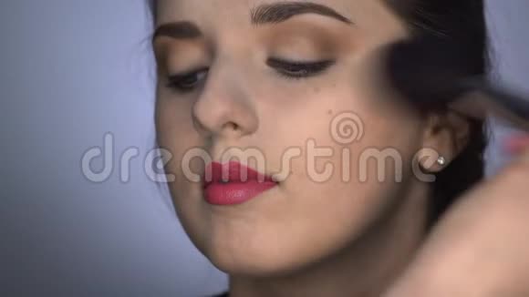 为坐在工作室的漂亮漂亮女人做专业化妆的过程化妆师使用粉末视频的预览图