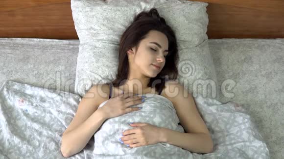 一个年轻的女人睡在被子下一个女孩躺在他房间的床上从上面看视频的预览图