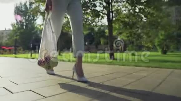 面目全非的女人拿着装有水果的棉网购物袋在避暑公园散步视频的预览图