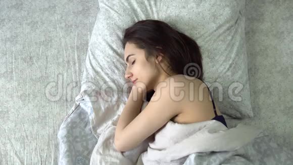一个年轻的女人睡在被子下一个女孩躺在他房间的床上从上面看视频的预览图