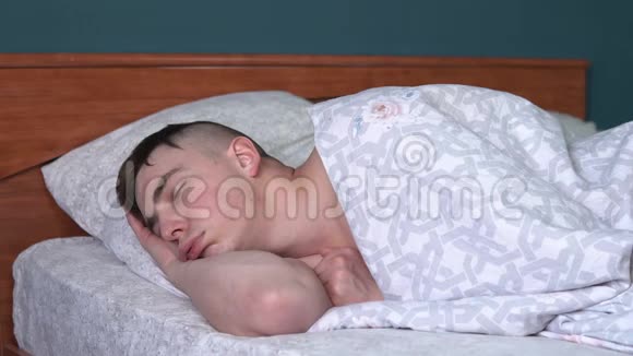 一个年轻人正在睡觉脸上有一种滑稽的表情一个人躺在他房间的床上视频的预览图