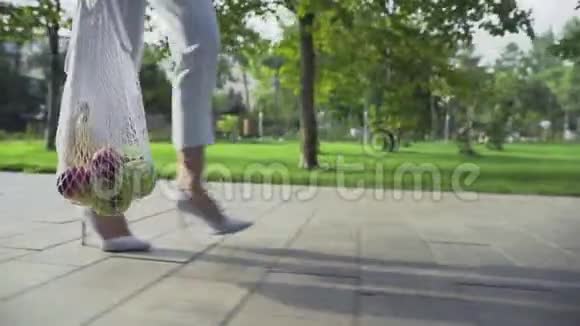 贴身女人拿着带水果的棉网购物袋在夏日公园散步视频的预览图