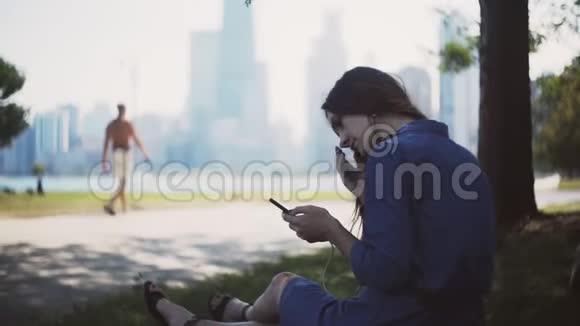 年轻漂亮的女人坐在公园的草地上用智能手机女人一个人在市区待过视频的预览图