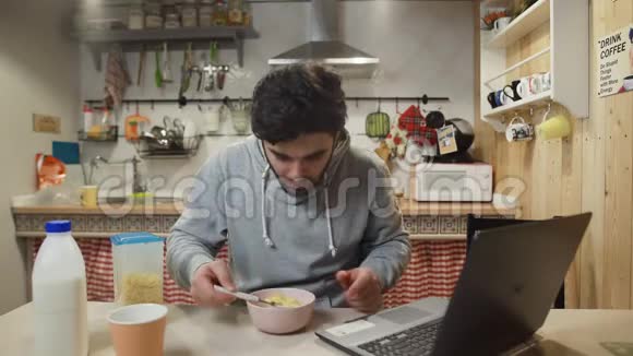 在家厨房里用笔记本电脑吃玉米片麦片粥的商人视频的预览图