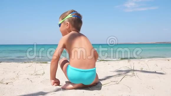 快乐的小男孩在雪白的沙滩上享受着绿松石的大海视频的预览图