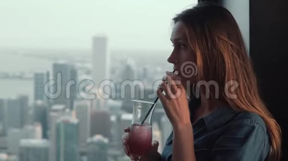 美国芝加哥一位年轻美丽的沉思女性站在摩天大楼的窗户附近喝着鸡尾酒的肖像视频的预览图