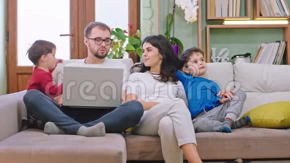 年轻漂亮的一家人坐在沙发上呆在家里隔离他们在一起玩聊天玩得很开心视频的预览图