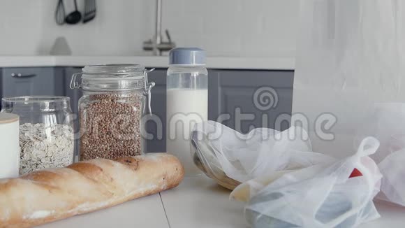 在厨房的木桌上把装有面包燕麦片荞麦牛奶蔬菜和水果的未包装购物袋关上视频的预览图