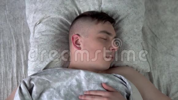 一个年轻人睡在被子下一个人躺在他房间的床上从上面看视频的预览图