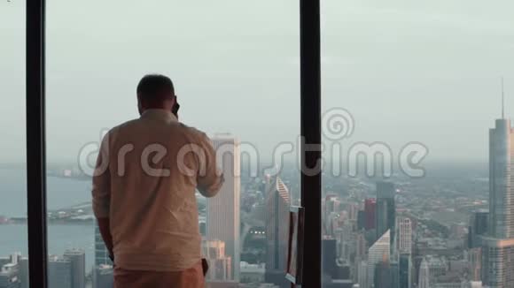 美国芝加哥摩天大楼的窗户附近站着一位年轻英俊的男子用手机交谈视频的预览图