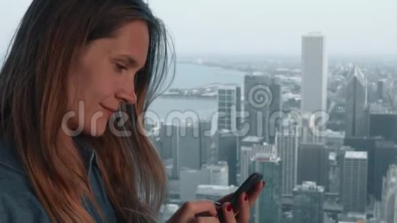 年轻的黑发女人站在摩天大楼的窗户附近使用智能手机美国芝加哥全景视频的预览图