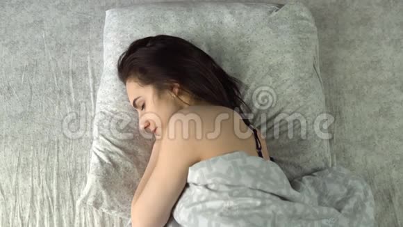 年轻女子醒来拿起电话一个女人从枕头下掏出一部智能手机从上面看视频的预览图