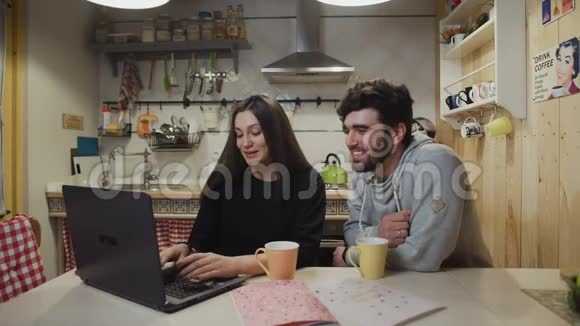 微笑的夫妇在厨房喝咖啡快乐的一对看手提电脑快乐的男人和女人说话视频的预览图