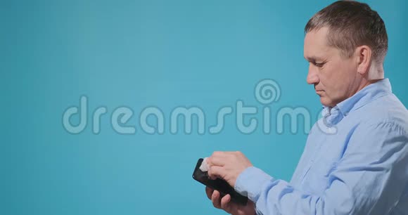 穿蓝色衬衫的老人用餐巾纸消毒智能手机视频的预览图