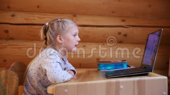 可爱的白种人小金发女孩坐在办公桌上手提电脑在线视频聊天学校课程视频的预览图