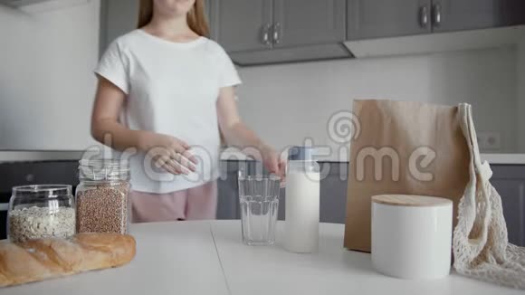 穿着白色连衣裙的年轻女子把牛奶从老式的瓶子倒进桌子上的玻璃杯里这是一个面目全非的女人视频的预览图
