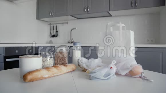 厨房木制桌子上有面包燕麦片荞麦牛奶蔬菜和水果的未包装购物袋青年视频的预览图