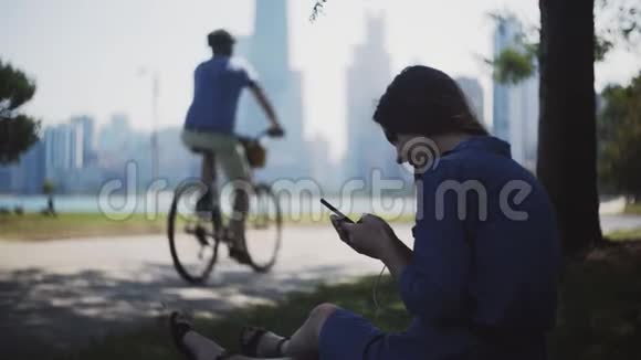 快乐的女人夏天坐在公园里用智能手机迷人的女性在市中心度过闲暇时光视频的预览图