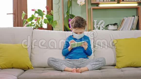 5岁的男孩在家中玩的时候他集中了一个玩智能手机的游戏同时坐在沙发上的概念视频的预览图