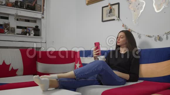 年轻漂亮的女人坐在沙发上用智能手机进行视频聊天视频的预览图