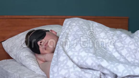 一个年轻人睡在睡眠面具里一个人躺在他房间的床上视频的预览图