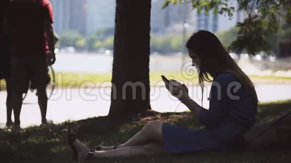 年轻漂亮的女人坐在公园的草地上用智能手机在美国芝加哥市中心休息的女性视频的预览图