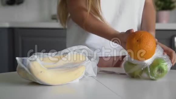 靠近的年轻女子把水果从塑料袋移到厨房木桌上可重复使用的网袋零废弃物视频的预览图
