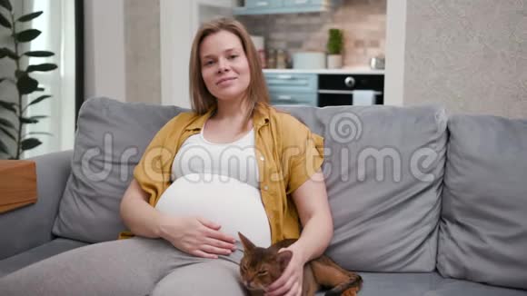 可爱和可爱的20年代微笑的女人坐在沙发上享受猫的乐趣视频的预览图