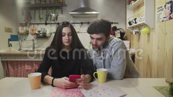年轻夫妇在厨房吃早餐快乐的一对看智能手机屏幕快乐的男人和女人说话视频的预览图