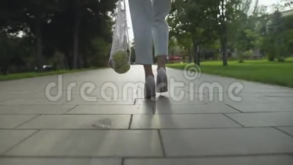 年轻女子穿着蓝色裤子和白色鞋子背着带水果的棉网购物袋走在里面视频的预览图