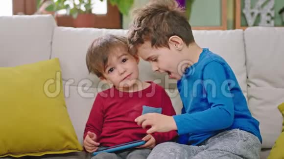 漂亮又有趣的小男孩坐在相机前的沙发上用智能手机视频的预览图