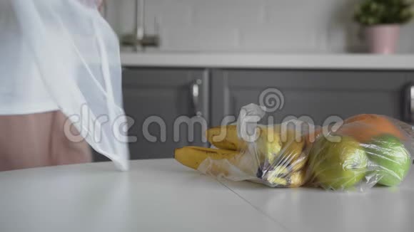 靠近的年轻女子把水果从塑料袋移到厨房木桌上可重复使用的网袋零废弃物视频的预览图