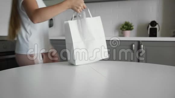 年轻的女人在木制桌子上的厨房里打开购物袋里面放着蔬菜零废家和生态袋生态视频的预览图