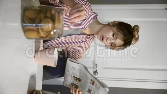 年轻美丽的黑发女人在厨房里喝咖啡吃饼干看报纸的垂直视频视频的预览图